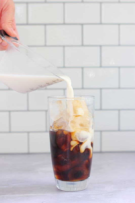 milk being poured over iced coffee