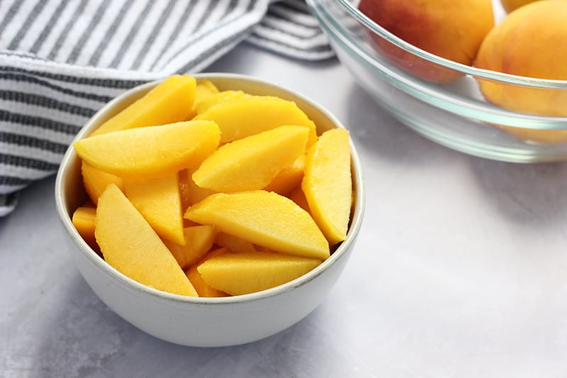 sliced peeled peaches stacked inside a white bowl.