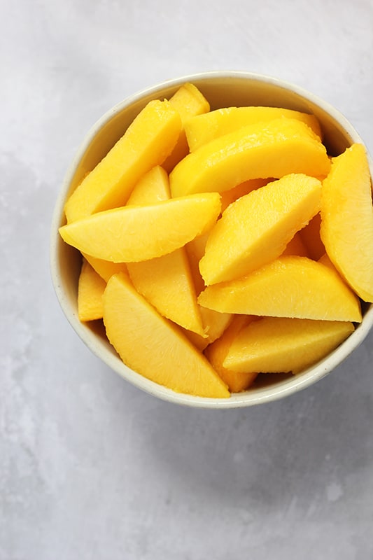 fresh peaches peeled and sliced, stacked inside white bowl.