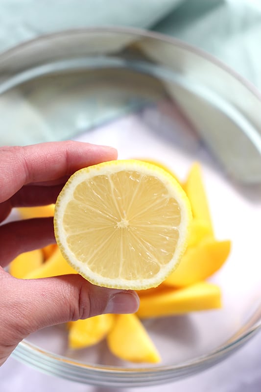 lemon slice being held by hand over bowl of sliced peaches