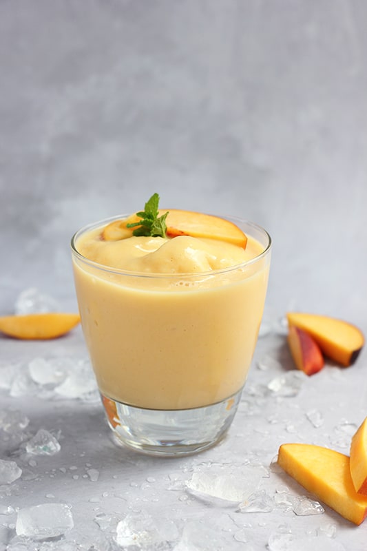 homemade peach smoothie in short glass on white table