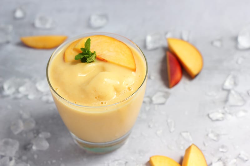 peach smoothie in glass with slices of peach on top