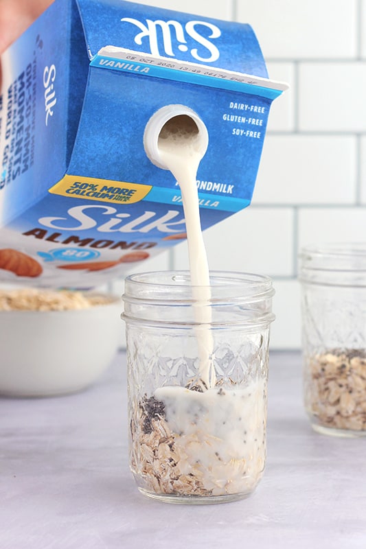 milk being poured over oats in mason jar