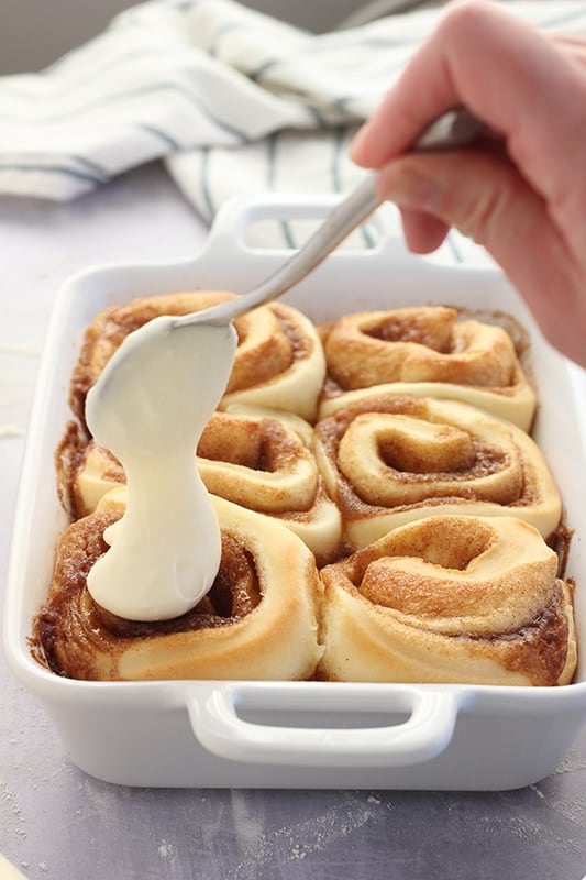 Frosting being spooned over warm cinnamon rolls