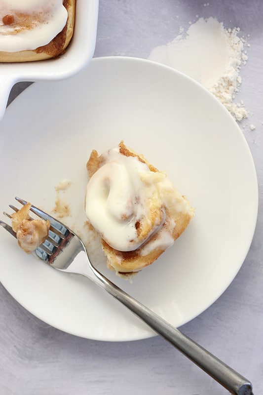 single cinnamon roll on a white plate with a bite on a fork