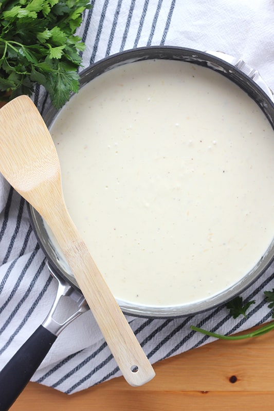 Top down image of a large and deep black skillet with a white sauce. A wooden spoon is balanced on the edge of the pan