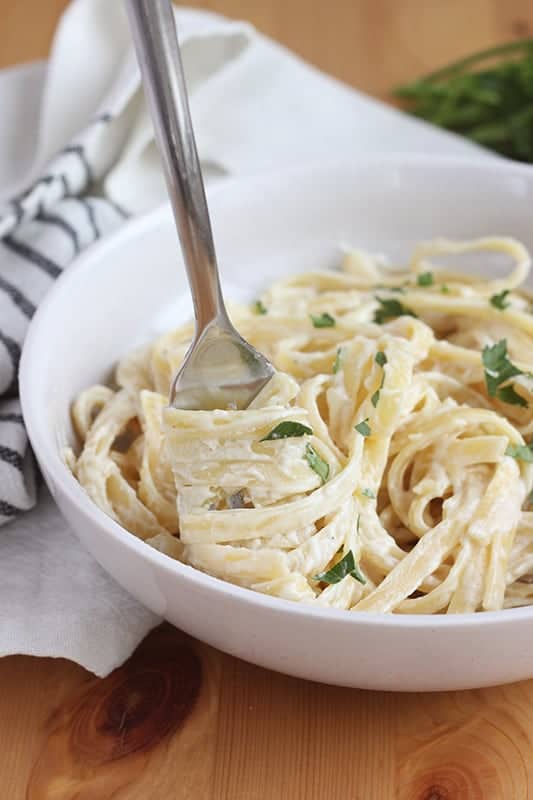 fork spinning Fettuccine into a spiral around the prongs in a white wide shallow bowl.