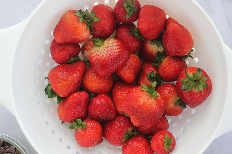 Top down image of fresh strawberries in a white strainer