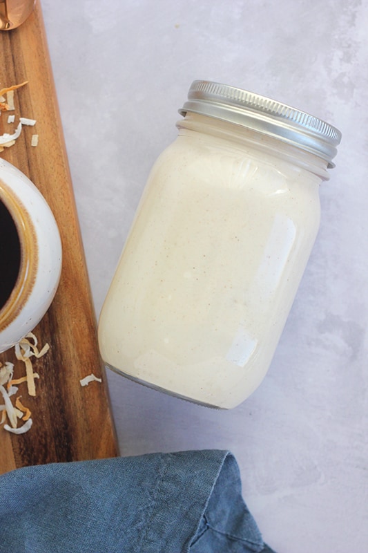 mason jar with a lid laying on a concrete color backdrop filled with coconut milk