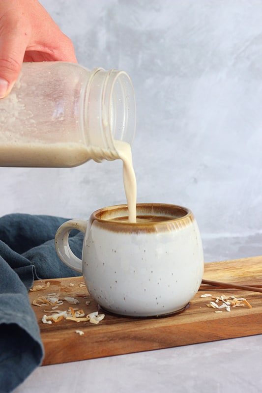 off white speckled short mug filled with espresso and coconut milk being poured in with a mason jar