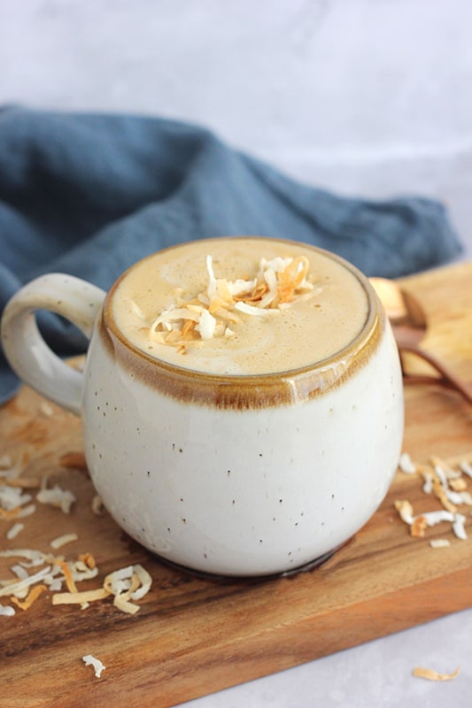 close up image of a short off white speckled mug filled with a latte that is topped with coconut flakes 