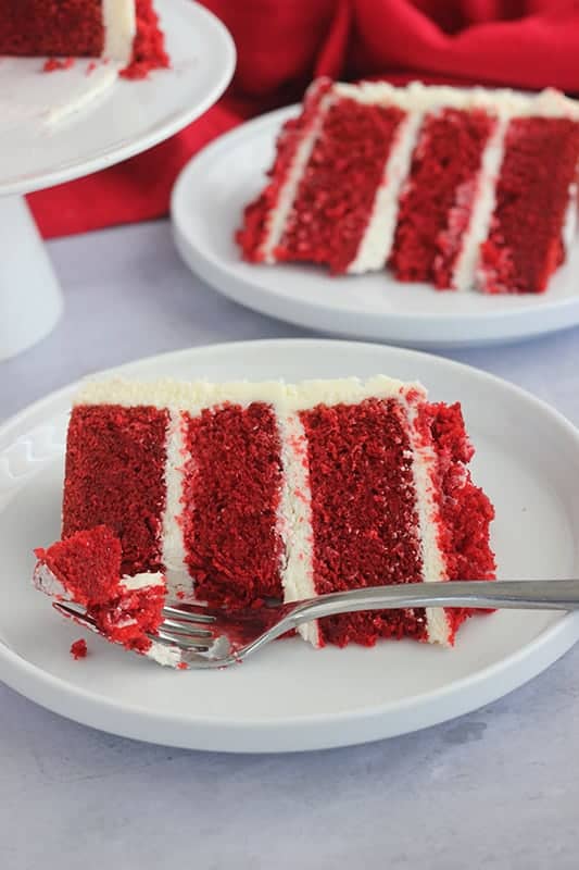 Slice of red velvet cake on a white plate with a bite on fork