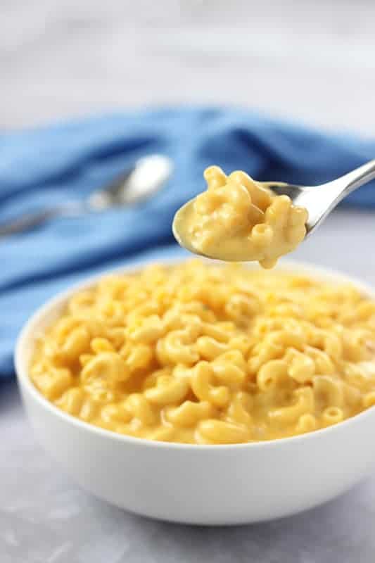 Bite of slow cooker macaroni and cheese held on spoon above bowl