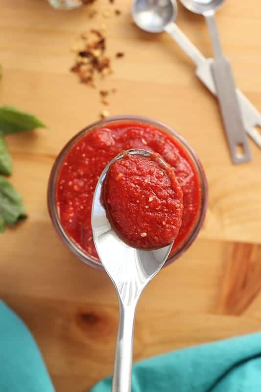 Pizza sauce in a mason jar with a spoonful held above the top