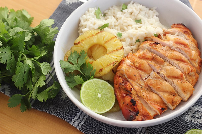 Bowl of Hawaiian chicken, pineapple, and rice with fresh cilantro and lime
