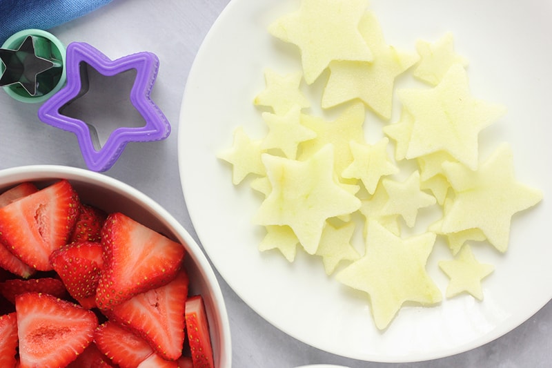 small white plate with dozens of apple slices cut into stars and a bowl filled with strawberry slices