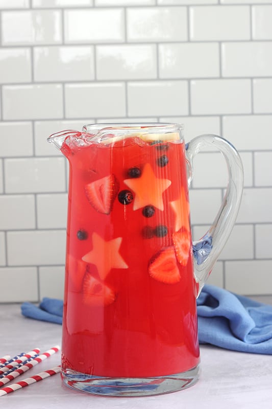 tall pitcher filled with red juice and floating strawberries, blueberries, and star shaped apple slices