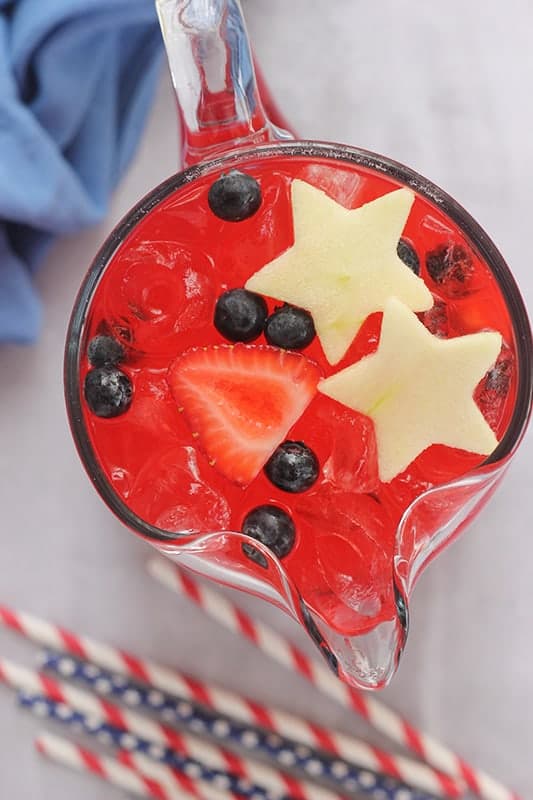 top down image of a pitcher filled with a red punch with red white and blue fruit on top