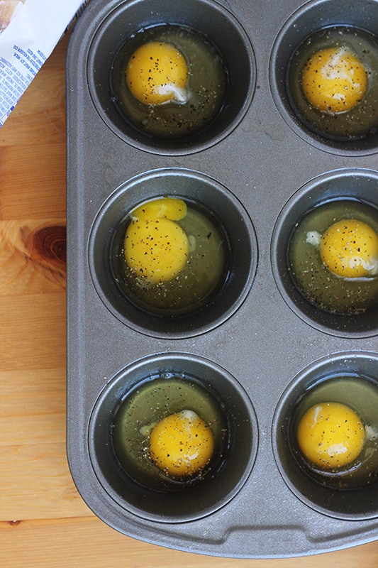 Eggs cracked into a muffin tin and seasoned with salt and pepper