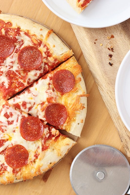 freezer pepperoni pizza that has been  cooked and sliced on a wooden table with a pizza cutter