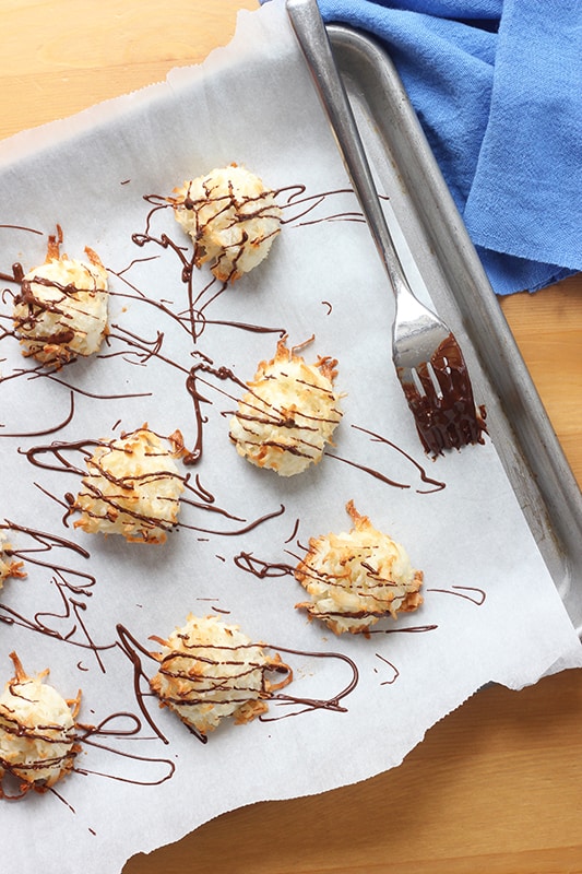 coconut cookies baked and sitting on a baking tray with chocolate being drizzled over with a fork