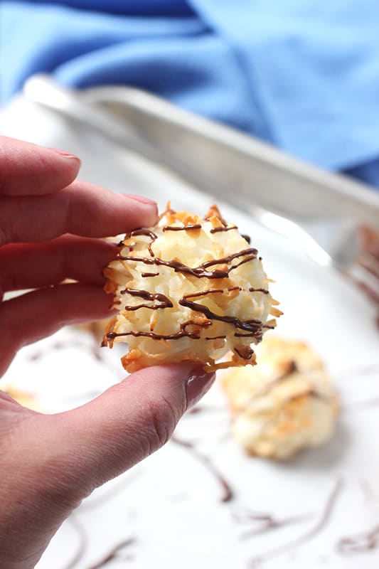 Single coconut macaroon held in hand over a baking tray