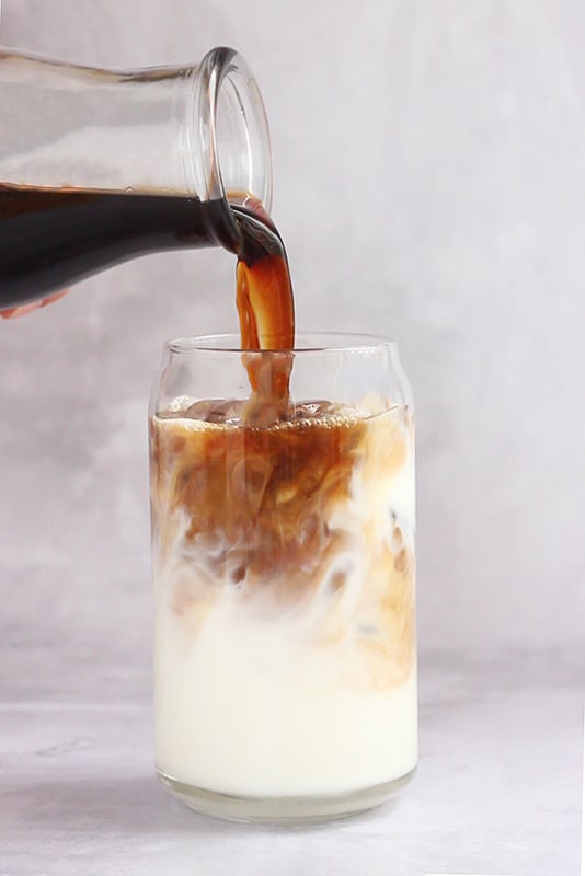 coffee being poured over milk in  a glass