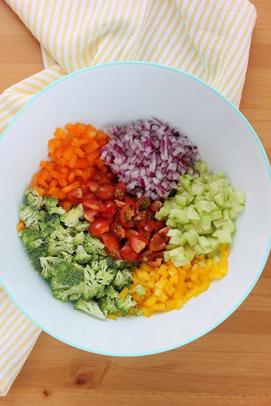 white mixing bowl filled with layers of fresh vegetables ready to be stirred.