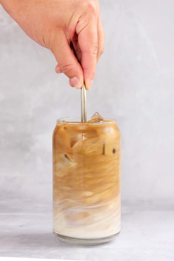 Hand holding a metal straw stirring an iced latte 