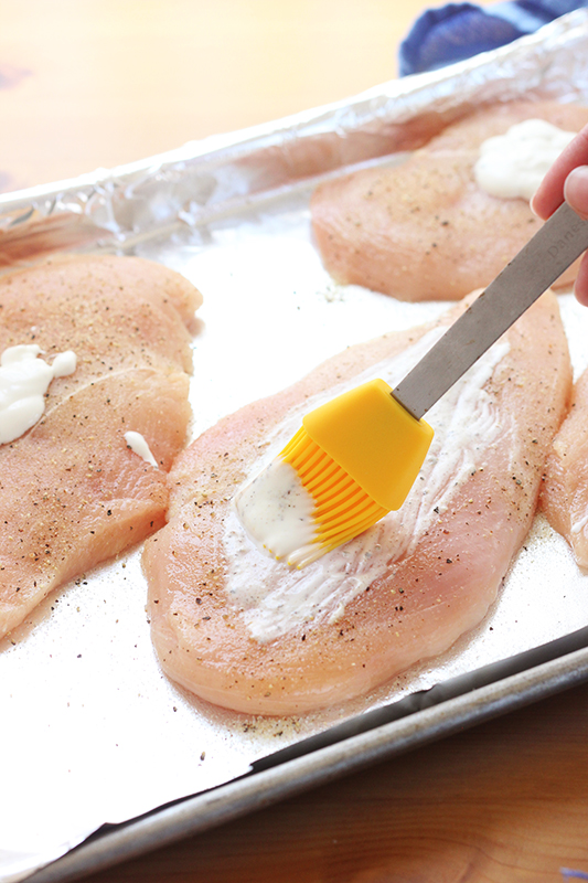 ranch dressing being brushed onto the top of chicken breast that is seasoned