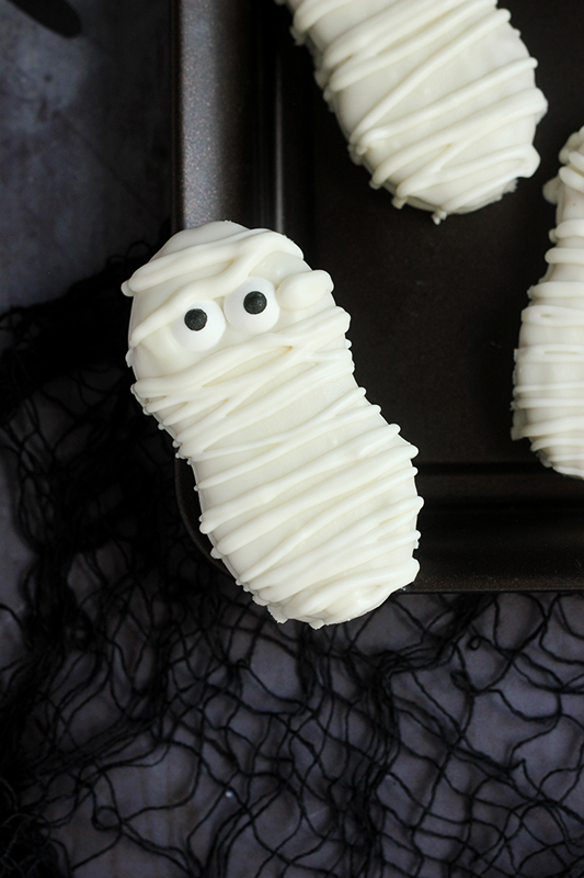 single cookie decorated to look like a mummy balancing on the edge of a black tray