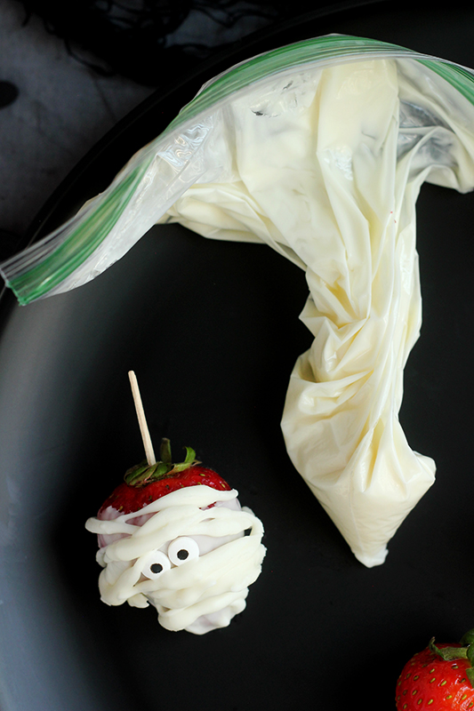 Finished strawberry mummy with a zip top sandwich bag full of melted white chocolate