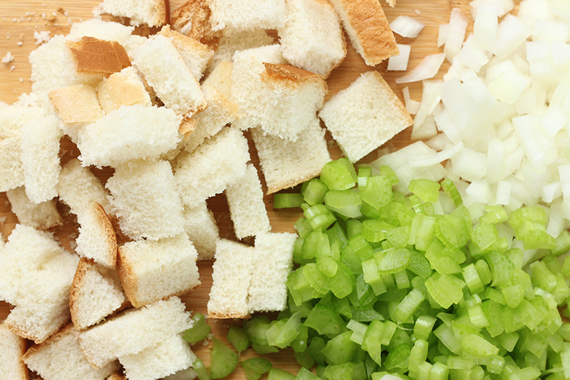 Chopped onion and celery on a cutting board with bread cubes