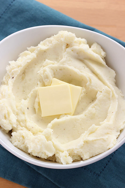 Mashed potatoes in a white bowl with tabs of butter resting on top