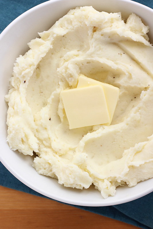 Mashed potatoes in a bowl with pats of butter on top