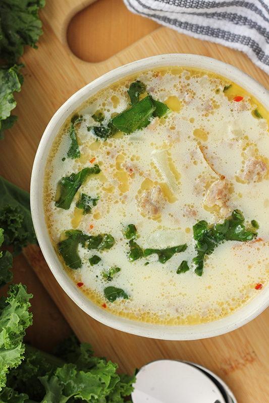 Zuppa Toscana soup in a white bowl on a cutting board surrounded with extra fresh kale