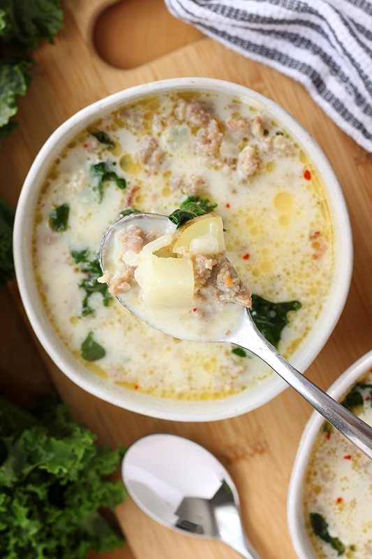 Bowl of soup with sausage, potatoes, and kale with a bite full in a spoon