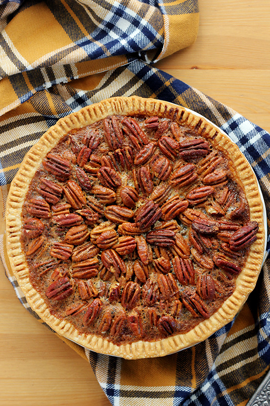 Top down photo of a pecan pie on top of a brown table top with a plaid napkin