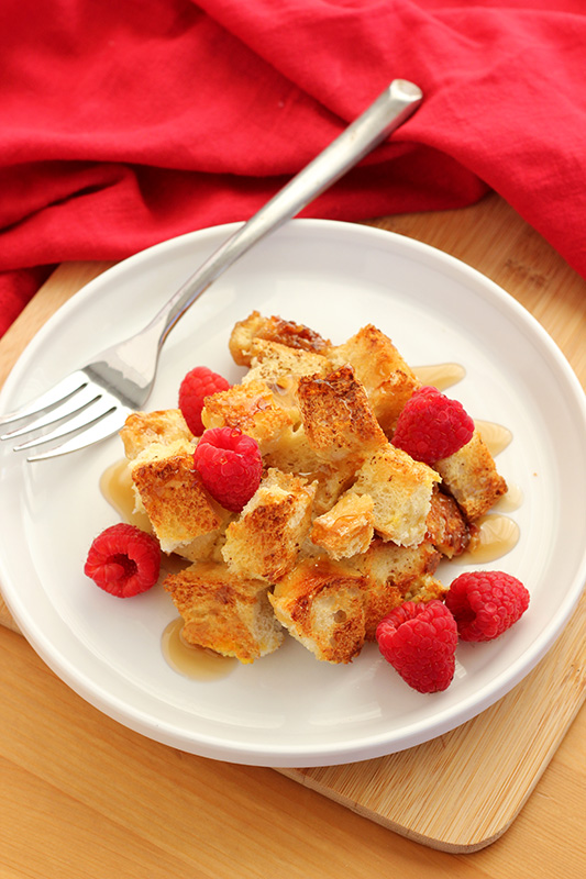 french toast casserole with syrup and raspberries on a white plate