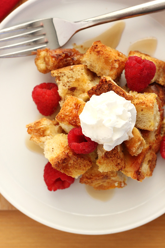 serving of french toast on a white plate with raspberries and a dollop of whipped cream