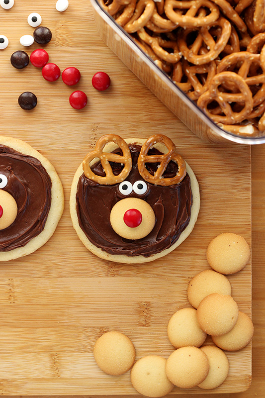 decorated reindeer cookie on a table top with a bowl of pretzels and m&M candies