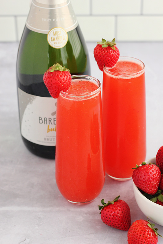 two glasses of strawberry punch with fresh berries and a bottle of champagne in the background.