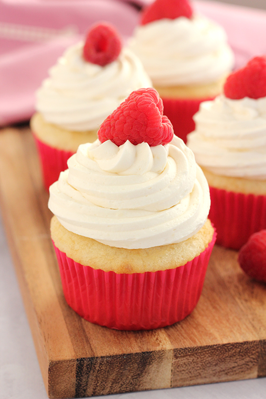 cupcakes on a wood platter in pink liners and topped with fresh raspberries