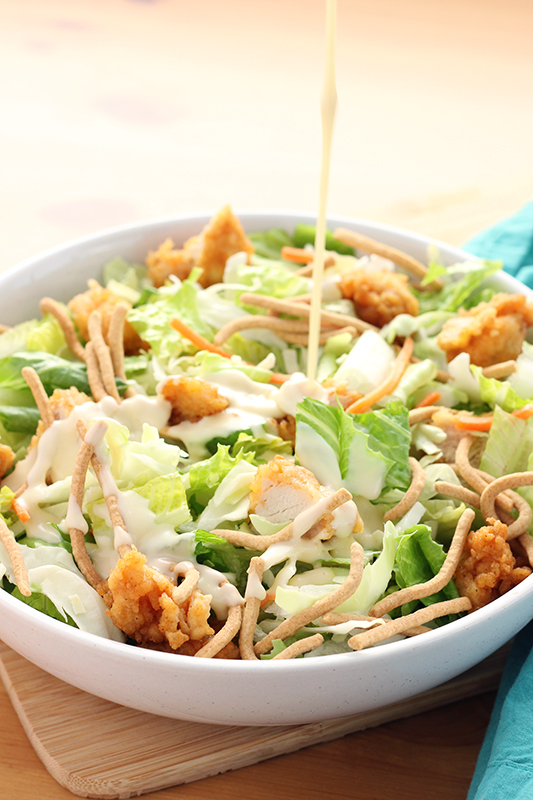 crispy chicken salad being drizzled with salad dressing