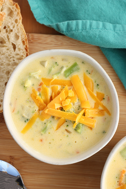 close up of cheese broccoli soup in a white bowl on a wooden table