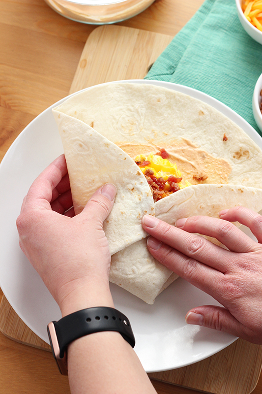hands folding a tortilla filled with eggs and bacon