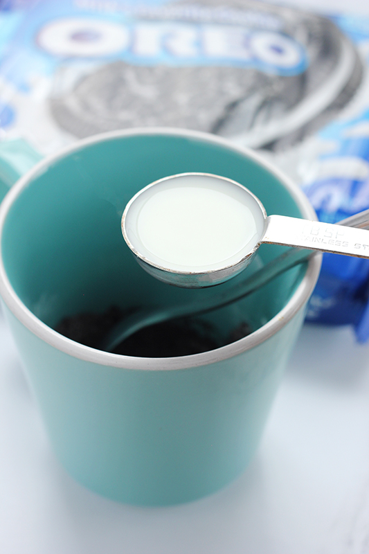 milk in a measuring spoon over the top of a blue mug