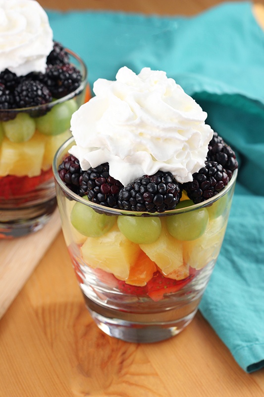 glass filled with layers of colorful fruit and topped with whipped cream