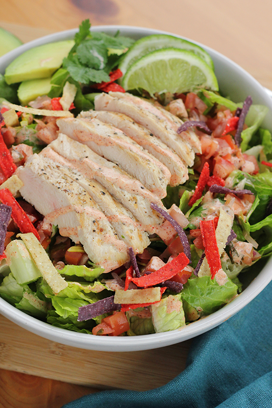 Close up photo of grilled chicken that is stacked on top of a salad in a white bowl