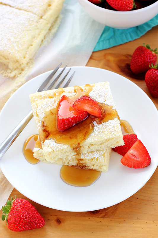 two pancake squares on a white plate topped with fresh strawberry slices and syrup